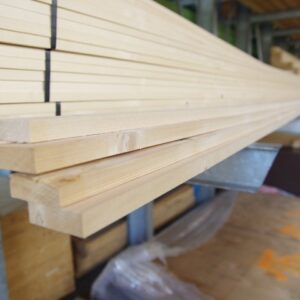 Gestapelte Holzplanken in einem Lager oder Baumarkt, die auf Metallträgern liegen.