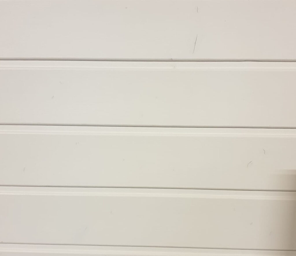 Weiße Profilleisten aus Fichtenholz mit einem Muster und einem Schild in der rechten unteren Ecke, das "Profilholz Fichte Weiß deckend" anzeigt.