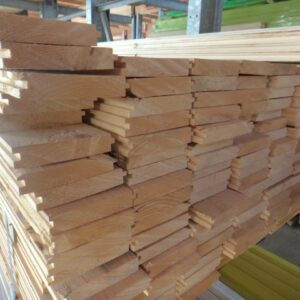Ein Stapel gehobelter Holzplanken mit Nut- und Federprofil liegt dicht gestapelt auf einer Palette in einer Lagerhalle.