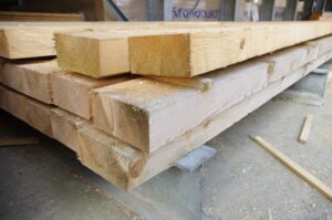 Gestapelte Holzbalken in einem Lagerraum auf einem Betonboden liegend.