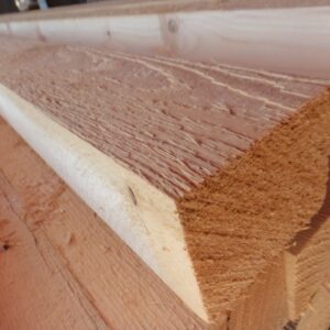 Nahaufnahme von langen Holzbohlen mit rauer Oberfläche, die gestapelt in einem Holzlager liegen.