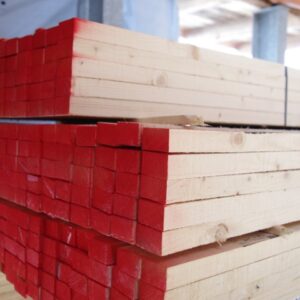 Ein Stapel Holzbretter mit rot gefärbten Enden in einem Lagerhaus oder auf einer Baustelle.