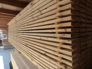 Ein Stapel von Holzbrettern, die in einem Lagerhaus lagern, mit gleichmäßigen Zwischenräumen zur Belüftung.