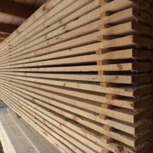 Gestapeltes Holz in einem Lager, bestehend aus langen, unbehandelten Holzbrettern, die horizontal gestapelt sind.