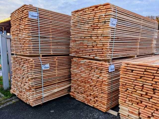 Gestapelte Holzbohlen in einem Lagerbereich, mit Metallbändern gesichert.