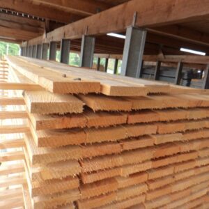 Gestapelte Holzbretter in einem überdachten Lager mit Metallstützen.