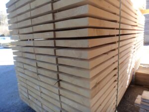 Ein Stapel Holzbohlen im Freien, ordentlich gestapelt und mit Bändern fixiert, in einer industriellen Umgebung.