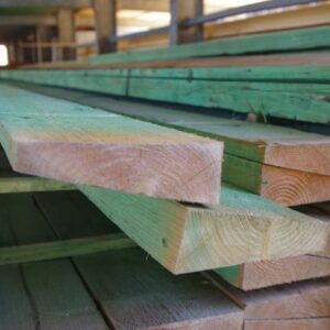 Gestapelte Holzbretter mit grünlicher Färbung, gelagert in einem Lagerraum.