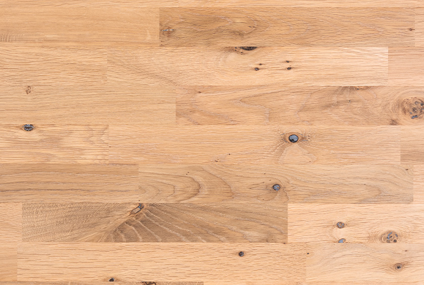 Holzoberfläche mit sichtbarer Maserung und einzelnen Astlöchern in verschiedenen Brauntönen.