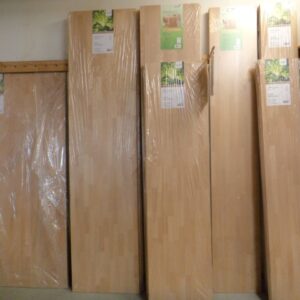 Mehrere große Holzplatten stehen aufrecht nebeneinander, in Plastikfolie verpackt, in einem Lager oder Geschäft für Holzprodukte.