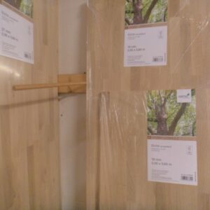 Holzplatten im Baumarktregal, einige mit Etiketten, die Details über Holzsorte und Maße anzeigen. Sichtbar sind europäische Eichenholzplatten in verschiedenen Dicken und Längen, in Plastikfolie verpackt.
