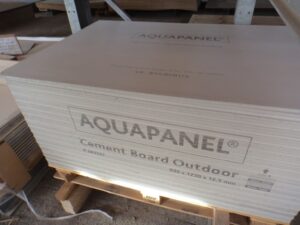 Stapel von Aquapanel-Zementplatten auf einer Holzpalette, beschriftet mit "Cement Board Outdoor" und Größenangaben.