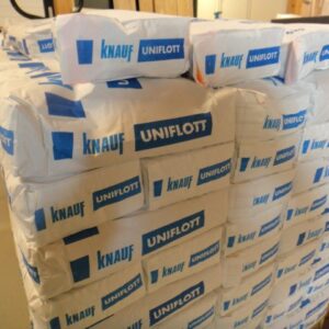 Mehrere Stapel von Knauf Uniflott Verputzmaterial in weißen Verpackungen mit blauer Aufschrift in einem Lagerraum.