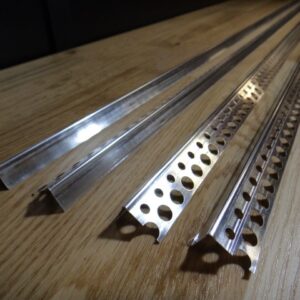 Nahaufnahme von vier Aluminiumprofilen mit unterschiedlich geformten und perforierten Kanten auf einer Holzoberfläche liegend.