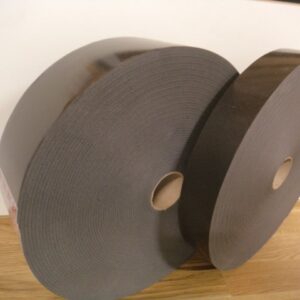Zwei große Rollen aus schwarzem Schaumstoffmaterial mit einer Pappröhre in der Mitte, auf einem Holzboden vor einer weißen Wand stehend.