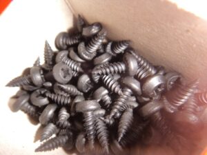 Eine Schachtel voller schwarzer Schrauben mit Kreuzschlitzköpfen.