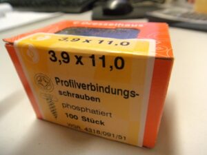 Eine orangefarbene Schachtel mit der Aufschrift "Profilverbindungsschrauben" in der Größe 3,9 x 11,0. Die Schachtel enthält 100 phosphatierte Schrauben."