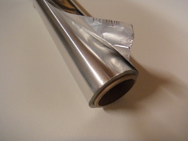 Eine Rolle Aluminiumfolie mit einem teilweise abgerollten Blatt auf einer hellen Oberfläche.