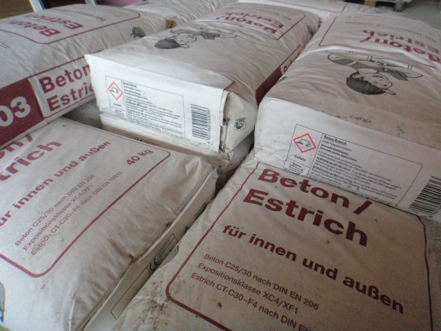 Säcke mit Beton/Estrich, beschriftet für den Einsatz innen und außen, jeweils 40 kg, in einem Lager gestapelt.
