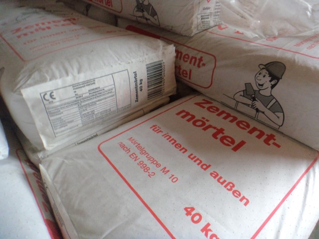 Ein Stapel von Säcken mit der Aufschrift "Zementmörtel" für Innen- und Außenanwendungen, 40 kg, mit einer Zeichnung eines Bauarbeiters auf der Verpackung.