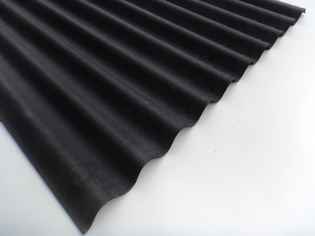 Schwarze, gewellte Dachplatte auf einer weißen Oberfläche.