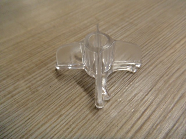Klares Kunststoffteil auf einem Holzuntergrund, geformt wie ein Miniaturflugzeug mit einer zentralen Öffnung.