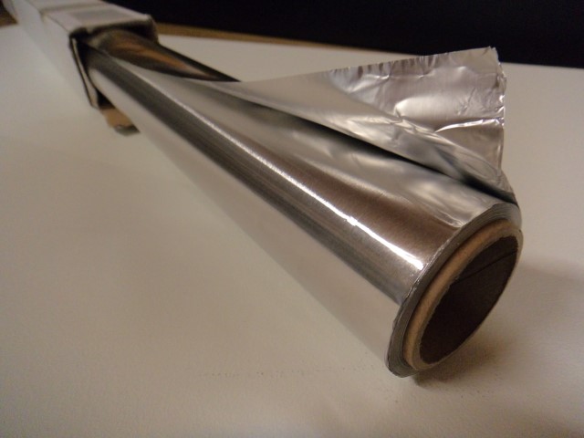 Eine Rolle Aluminiumfolie liegt auf einem Tisch, teilweise ausgerollt.