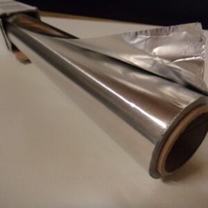 Eine Rolle Aluminiumfolie auf einem Tisch liegend, teilweise ausgerollt und glänzend.