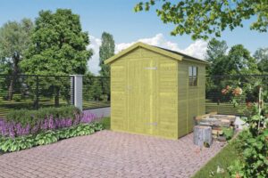 Ein hellgrünes Holzblockhaus mit Schrägdach steht auf gepflastertem Boden in einem Garten, umgeben von Blumenbeeten und Bäumen im Hintergrund.