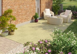 Gemütlicher Terrassenbereich mit zwei hellen Sesseln und einem Tisch auf einer gelben Matte, umgeben von Ziegelmauern und blühenden Pflanzen im Garten.