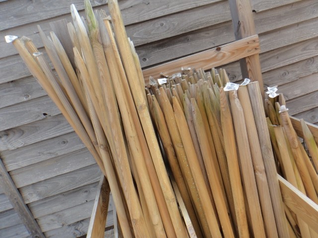 Ein Stapel von angespitzten Holzpfählen lehnt an einem Holzzaun.