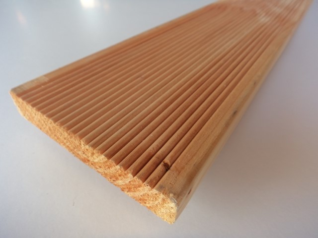 Nahaufnahme einer Holzbohle mit parallelen Rillen auf einer Seite, die auf einer weißen Oberfläche liegt.