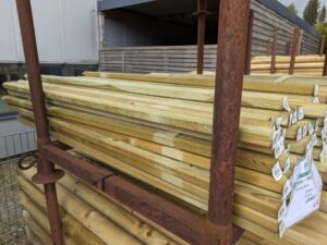 Ein Stapel holzbehandelter Bretter auf einem Metallgestell im Außenbereich, bereit für den Verkauf oder die Lagerung, mit Etiketten auf der Vorderseite versehen.