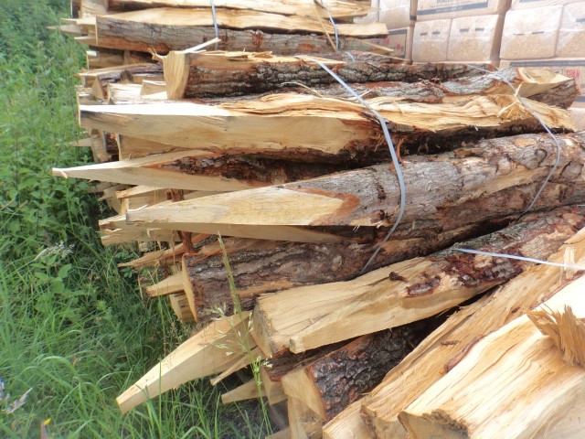 Gestapelte, zugespitzte Holzpfähle mit Rinde, die mit Draht gebündelt sind und auf Gras liegen, bereit zur weiteren Verwendung.