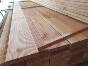 Stapel aus Holzbrettern mit sichtbarer Maserung und glatter Textur, wahrscheinlich zum Bauen oder für Handwerksarbeiten, in einem Innenraum gelagert.