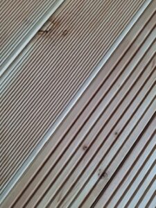 Nahaufnahme einer Holzterrasse mit diagonalen und parallelen Rillen in hellem Holzton.