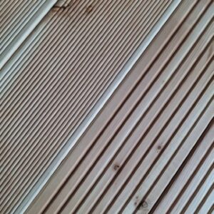 Nahaufnahme einer Holzterrasse mit diagonalen und parallelen Rillen in hellem Holzton.