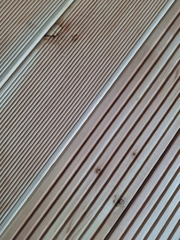 Nahaufnahme einer Holzterrasse mit diagonalen und parallelen Rillen in hellem Holzton.