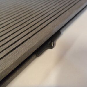 Nahaufnahme eines gerillten Terrassendielenprofils aus Holz oder Verbundmaterial mit einer darunterliegenden Halterung oder Clipsystem zur Befestigung.