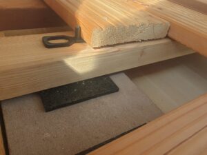 Unterkonstruktion aus Holz mit einem Gummipuffer zwischen zwei Holzbalken und einer schwarzen Metallhalterung, die die Balken verbindet.