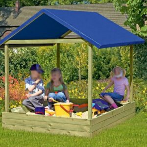 Drei Kinder spielen in einem Sandkasten mit blauem Dach in einem Garten, umgeben von blühenden Pflanzen und einem Rasen.