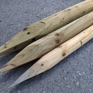 Drei spitze Holzpfähle liegen auf einer Asphaltoberfläche, die Holzmaserung ist deutlich sichtbar, und die Pfähle weisen einige Astknoten auf.
