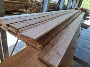 Ein Stapel von Holzdielen mit Nut-und-Feder-Profilen liegt gestapelt auf Regalen in einem Lagerraum.
