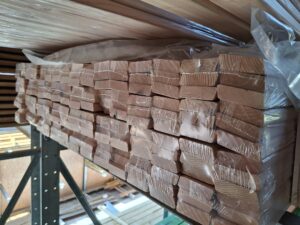 Gestapelte Holzlatten, die in Plastikfolie eingewickelt in einem Lager auf einem Metallregal gestapelt sind.
