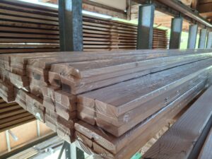 Gestapelte und in Folie eingewickelte Holzlatten in einer Lagerhalle aus Holz und Metallträgern.