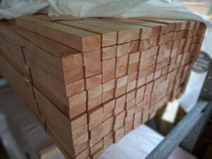 Ein Stapel schmaler Holzlatten, ordentlich gestapelt und auf einer Palette gelagert, mit Kunststofffolie bedeckt.