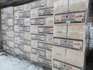 Gestapelte, verpackte Ballen von Peer Span Hobelspäne, auf Paletten im Freien gelagert, umgeben von Schnee.