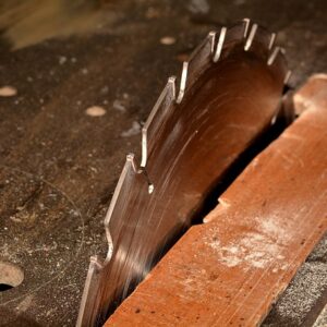 Nahaufnahme einer Kreissäge mit einem großen, gezahnten Sägeblatt, das aus einem Holztisch herausragt.