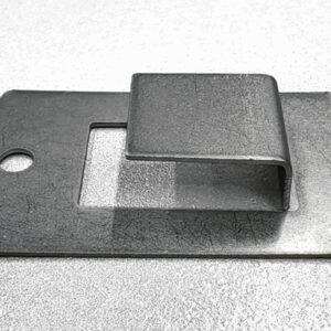 Ein rechteckiges Metallblech mit einem eingeschnittenen, erhobenen Abschnitt in der Mitte, das auf einer glänzenden Oberfläche liegt. Es hat ein rundes Loch auf der linken Seite.