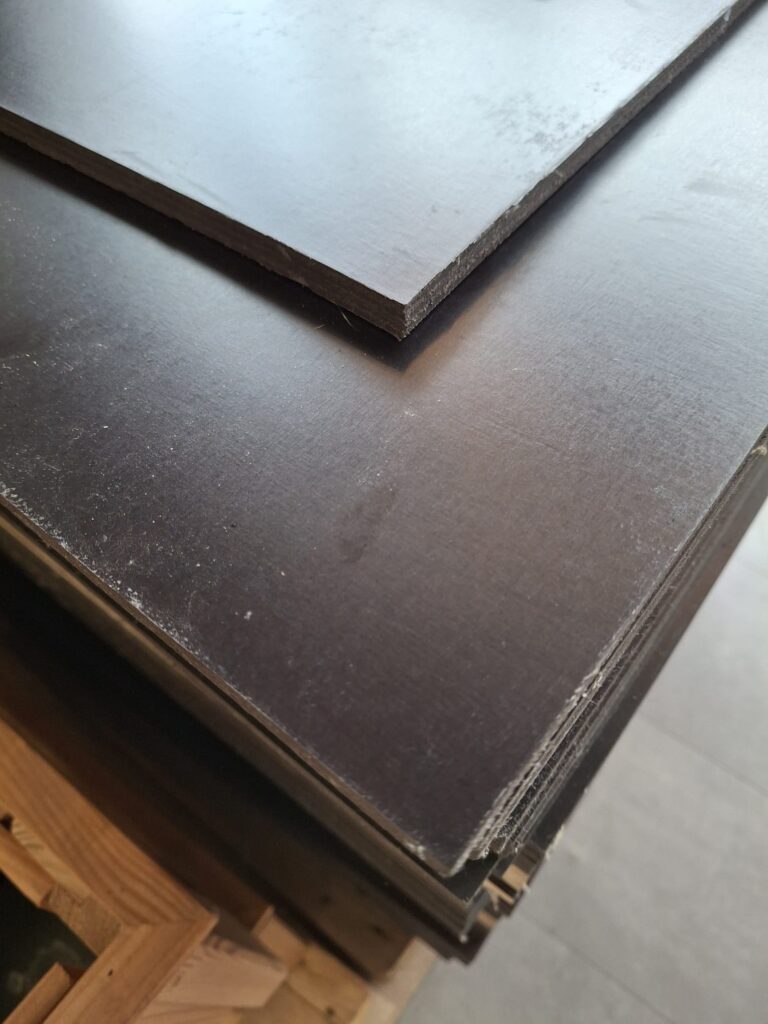 Stapel schwarzer, glatter Holzplatten auf einer Holzpalette.